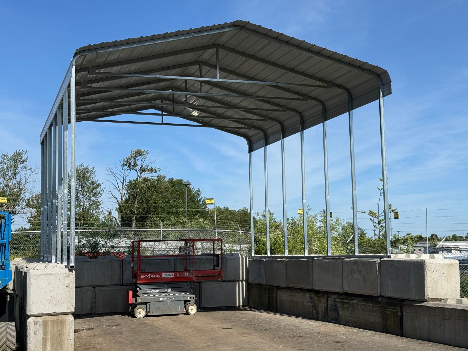 Large metal canopy over concrete barriers and a red work platform in an outdoor industrial yard