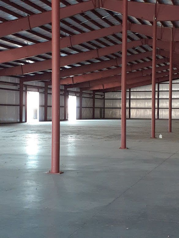 An expansive, empty warehouse with tall red metal support columns and a concrete floor under a metal frame ceiling.