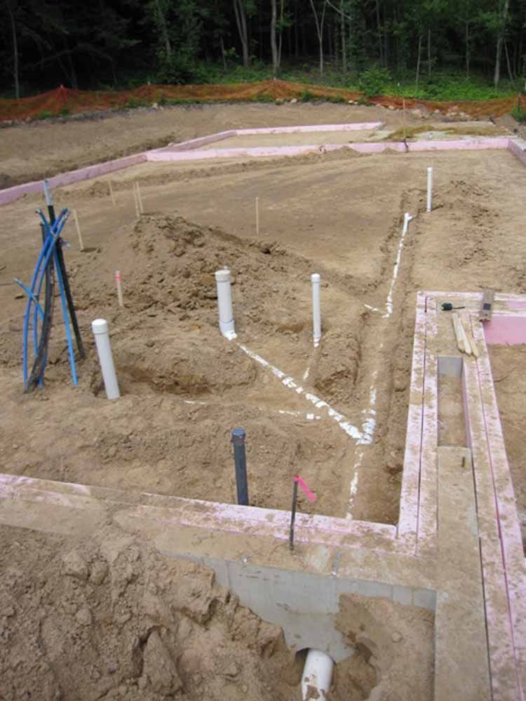 Construction site with plumbing pipes laid out in trenches, pink insulation outlining foundation.