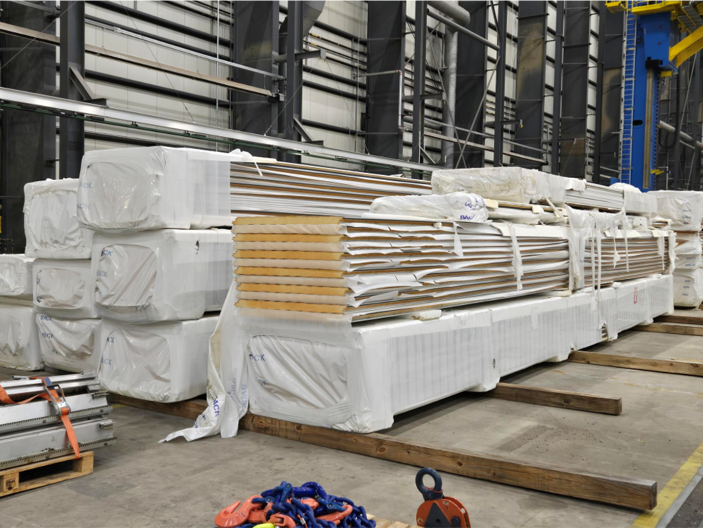 Stacks of packaged wooden panels in an industrial setting, wrapped in white plastic.
