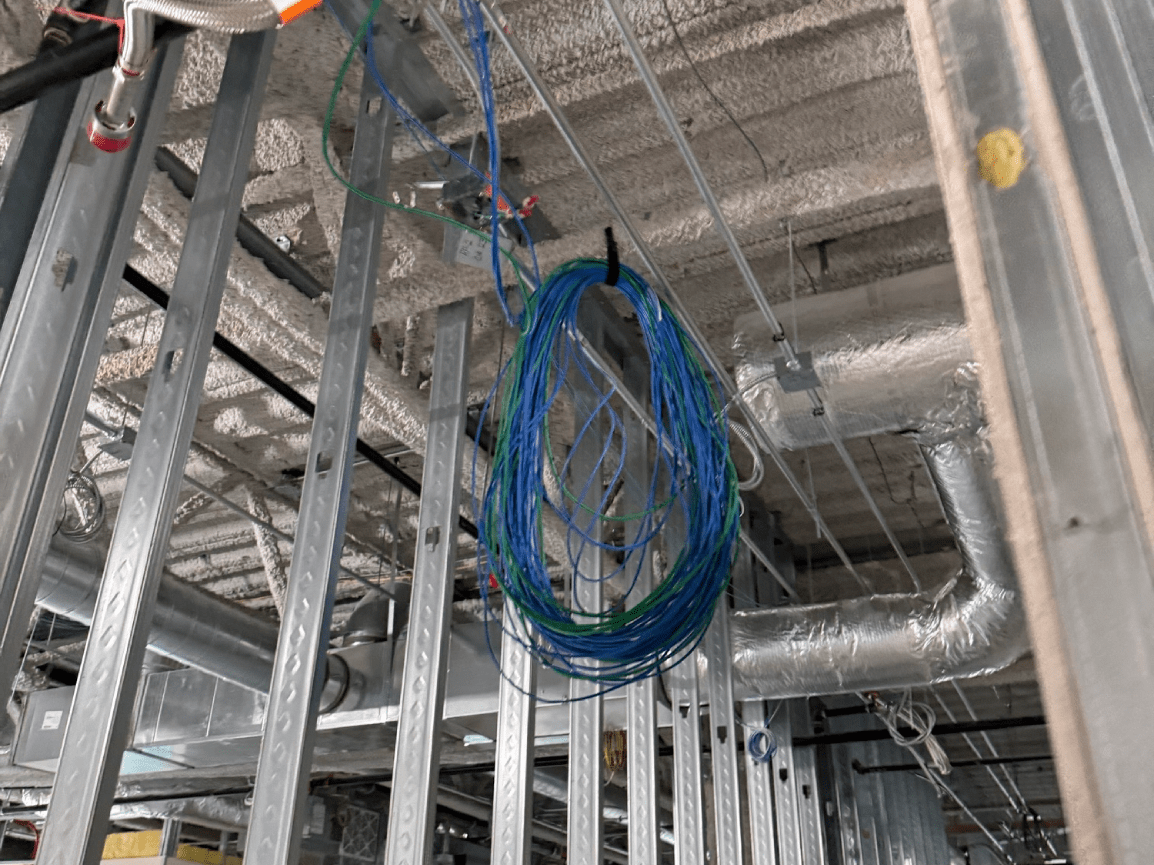 Coiled blue cable hanging in an unfinished industrial ceiling with exposed ducts and framing.