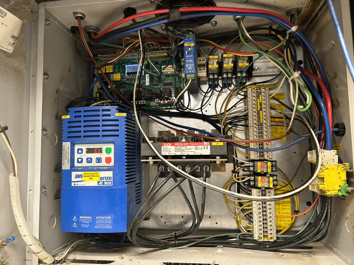 Open electrical control panel with blue inverter, wiring, circuit boards, and terminal blocks.