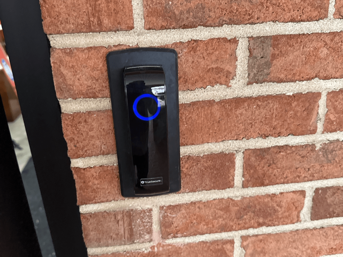 Black doorbell on a brick wall with a blue circular light indicator
