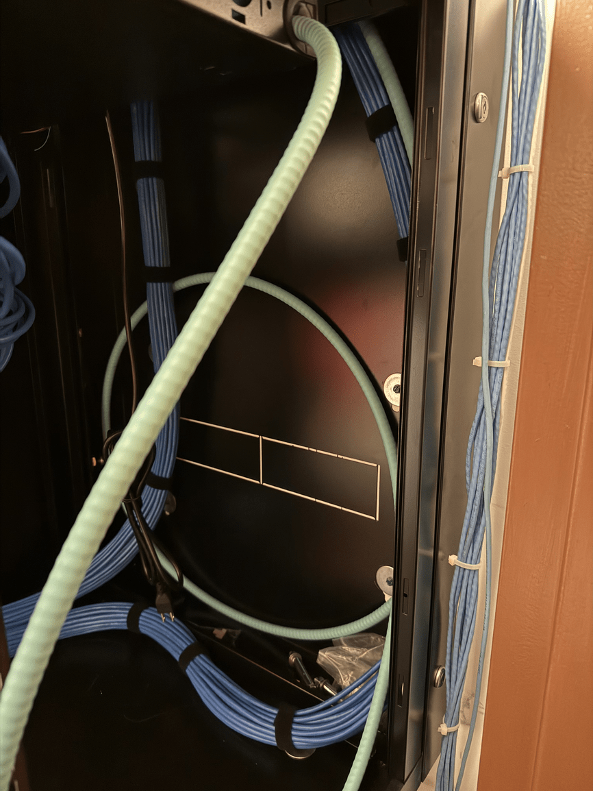 Network cables inside a wooden cabinet, with blue and green wires coiled around a black panel.