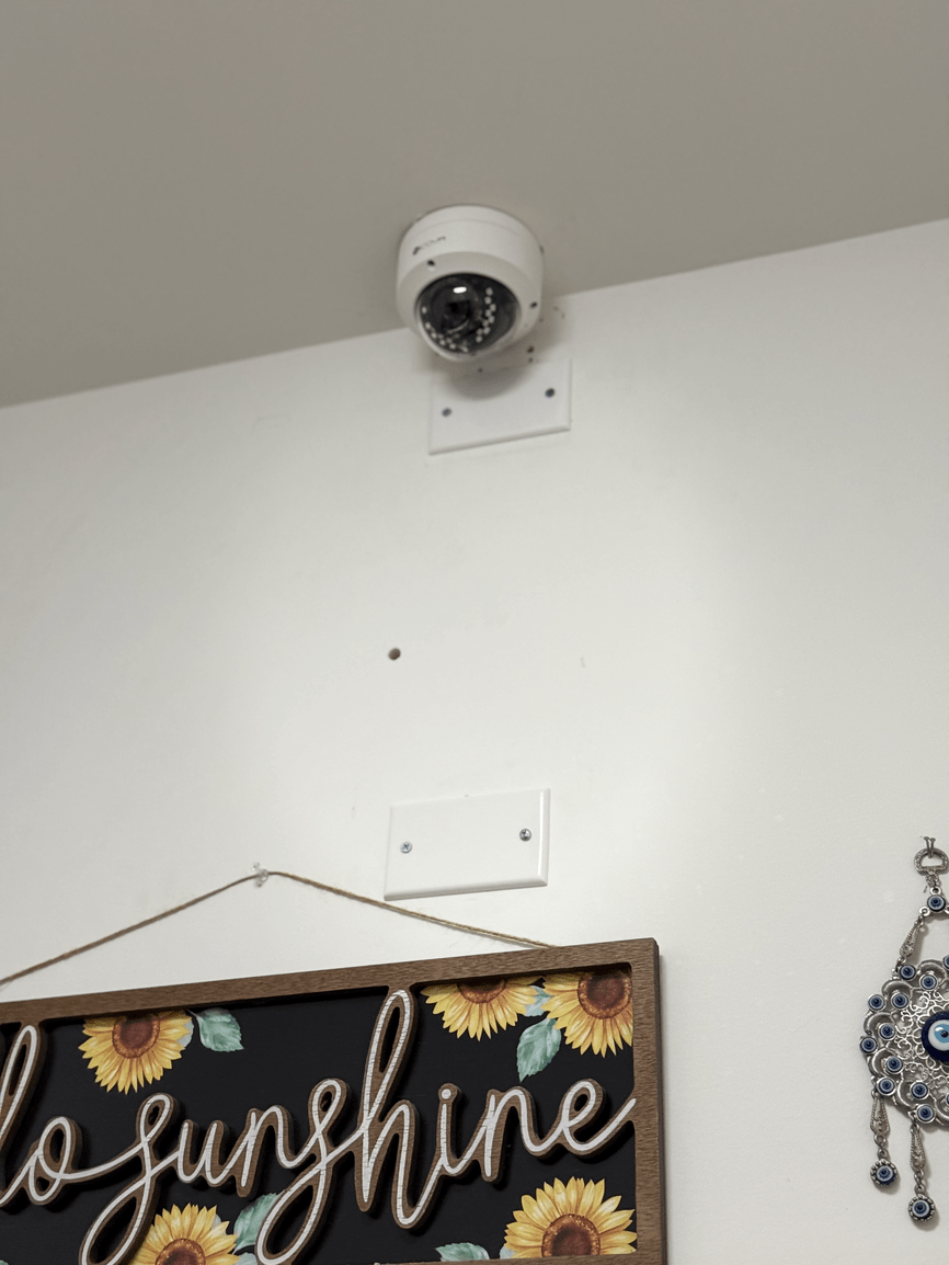 White wall with a dome security camera mounted above a decorative “sunshine” sign.
