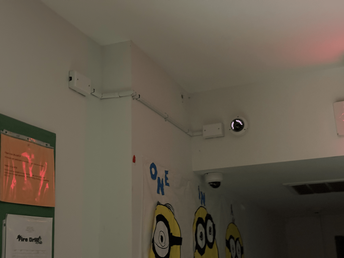 Wall corner with wiring, a security camera, and Minions wall art in a classroom-like room