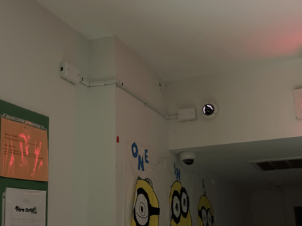 Wall corner with mounted security cameras, ceiling wiring, and Minions wall decals above a bulletin board.