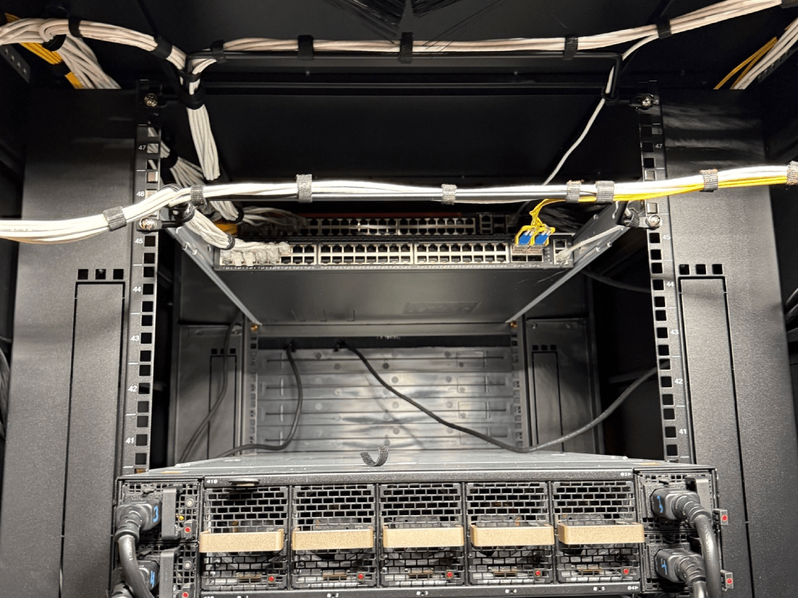 Open server rack with empty middle bay, cables, and equipment at the bottom under overhead wiring