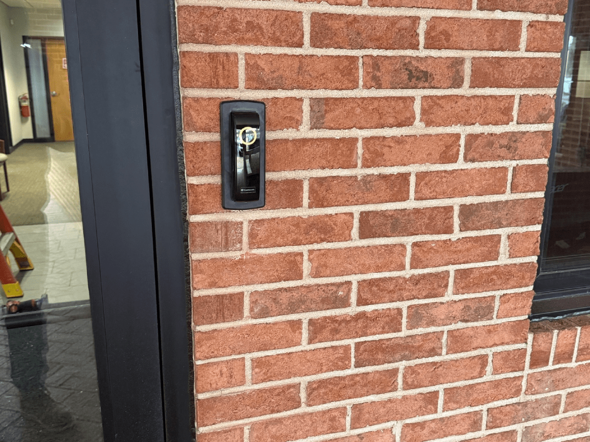 Brick wall with a black wall-mounted call button beside a doorway.