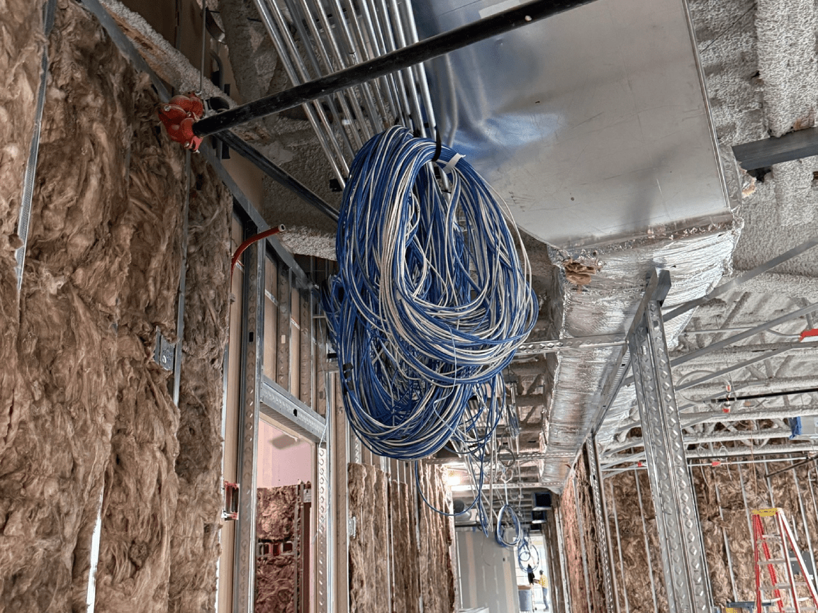 Coiled blue cable hanging from a metal beam in a partially finished interior space