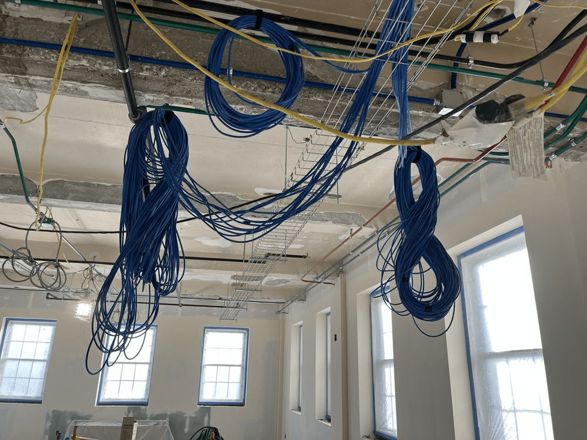 Blue cables hanging from the ceiling in an unfinished room with exposed wiring and windows