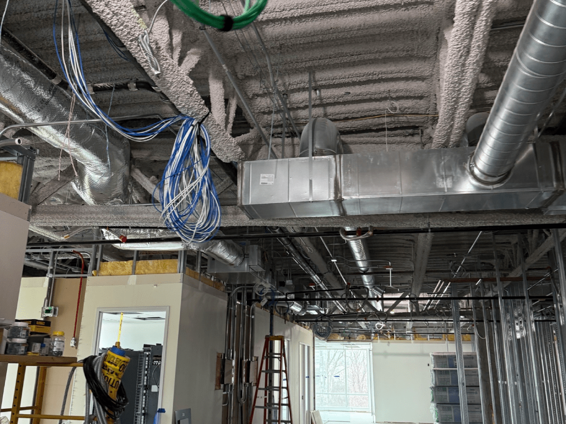 Unfinished commercial interior with exposed ductwork, wiring, and construction materials on the ceiling.