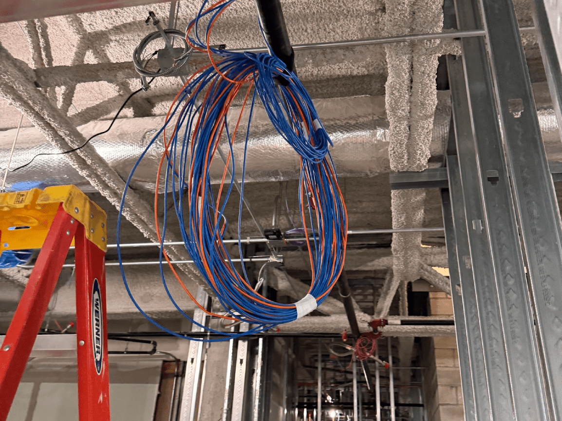 Coiled blue and orange cables hanging from the ceiling in a construction area.