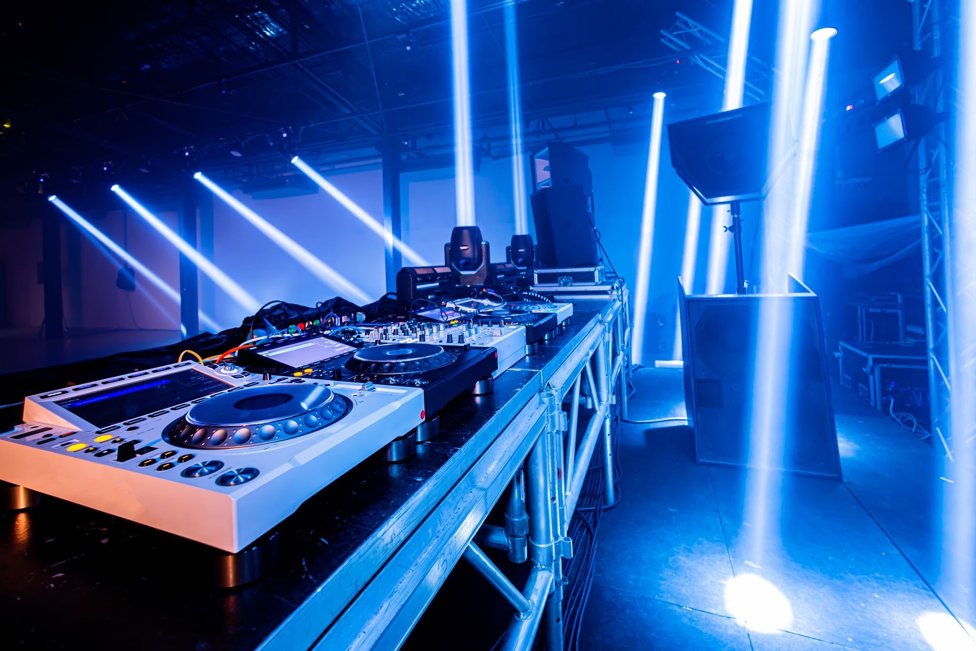 Blue-lit DJ booth with turntables and mixing equipment on a stage with bright light beams