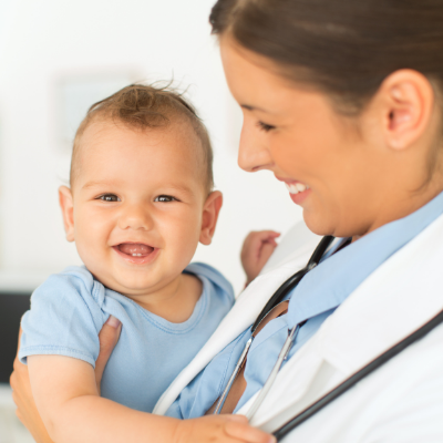 Smiling baby in a blue shirt with a doctor in a white coat and stethoscope