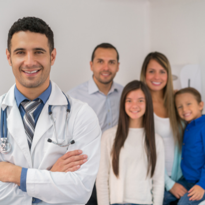 Doctor in white coat stands with smiling family in a bright clinic setting.
