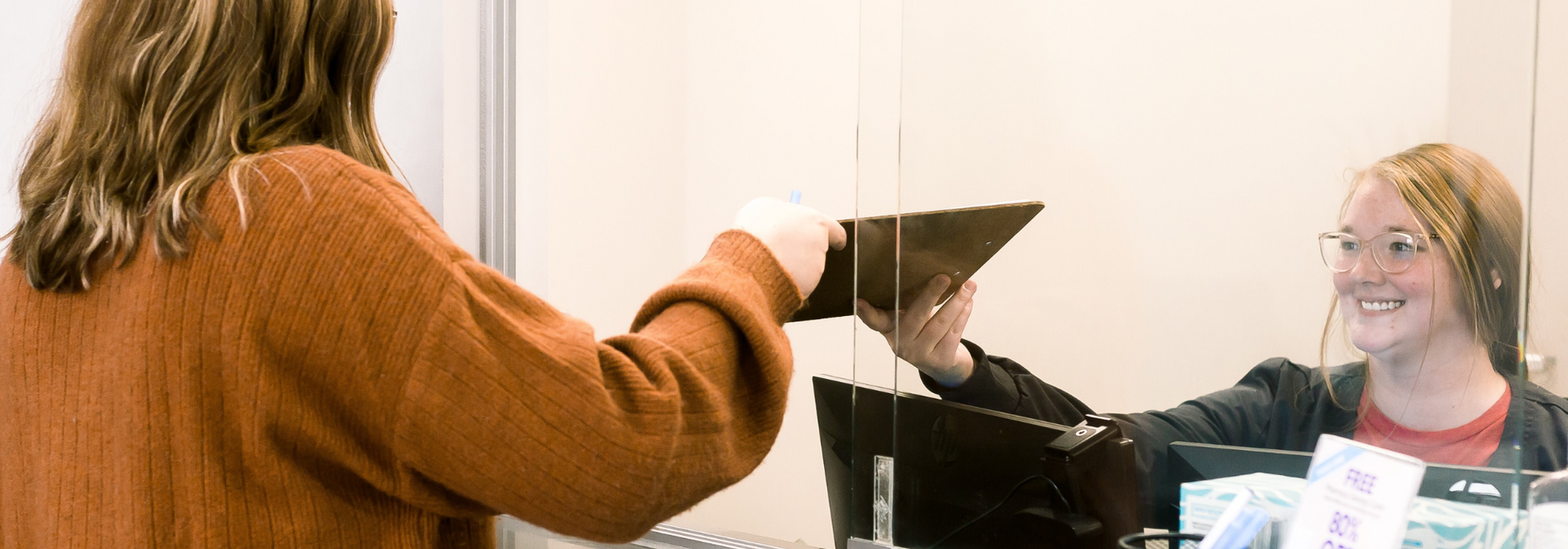 Woman handing documents across a counter to a smiling clerk in an office reception area