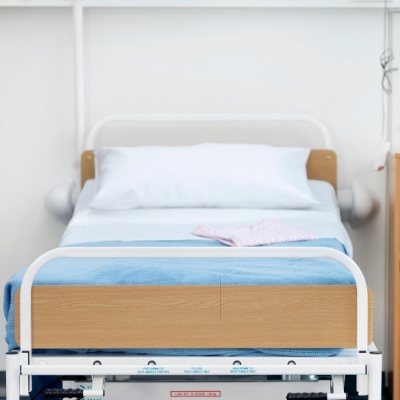 Hospital bed with white linens, blue blanket, and pink cloth in a bright room