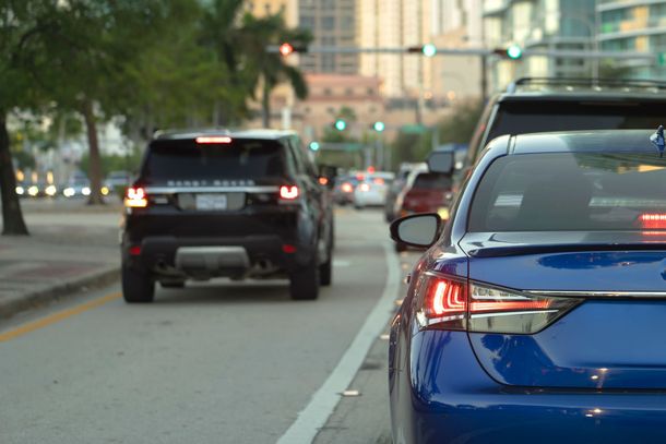Blue car parked on a city street behind a black SUV at dusk