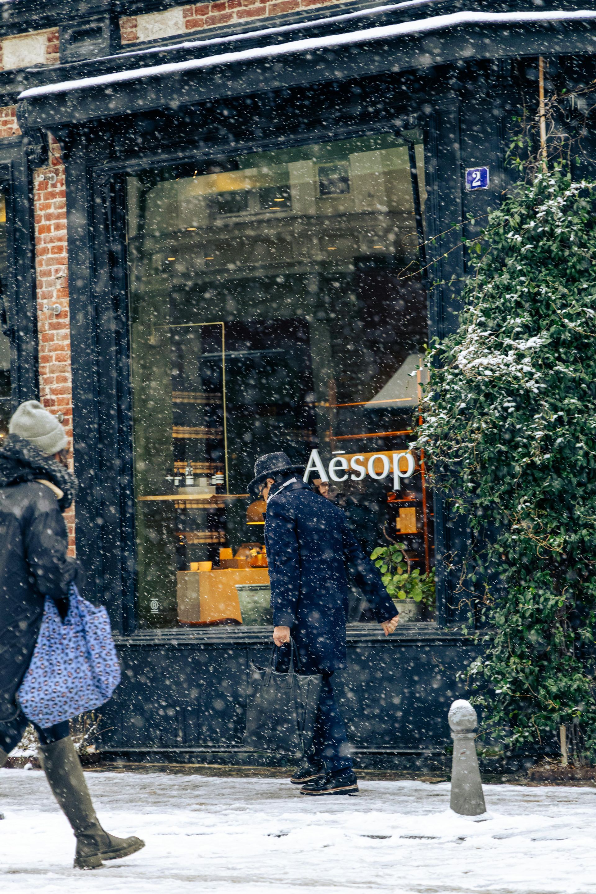 Snowy street scene outside Aesop store, with people walking past the window in winter coats
