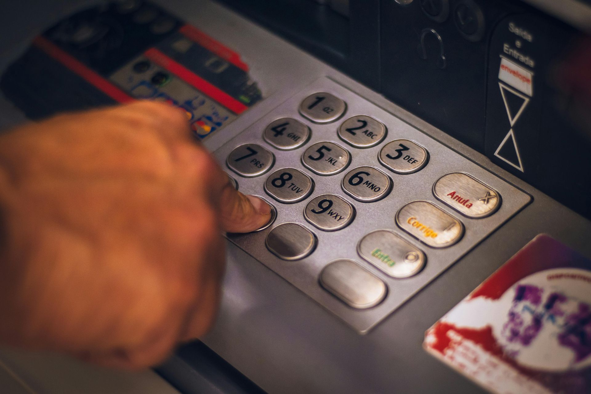 Hand pressing numbers on an ATM keypad with card slot and cash dispenser visible