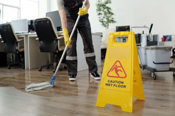 Custodian mopping office floor beside yellow caution wet floor sign