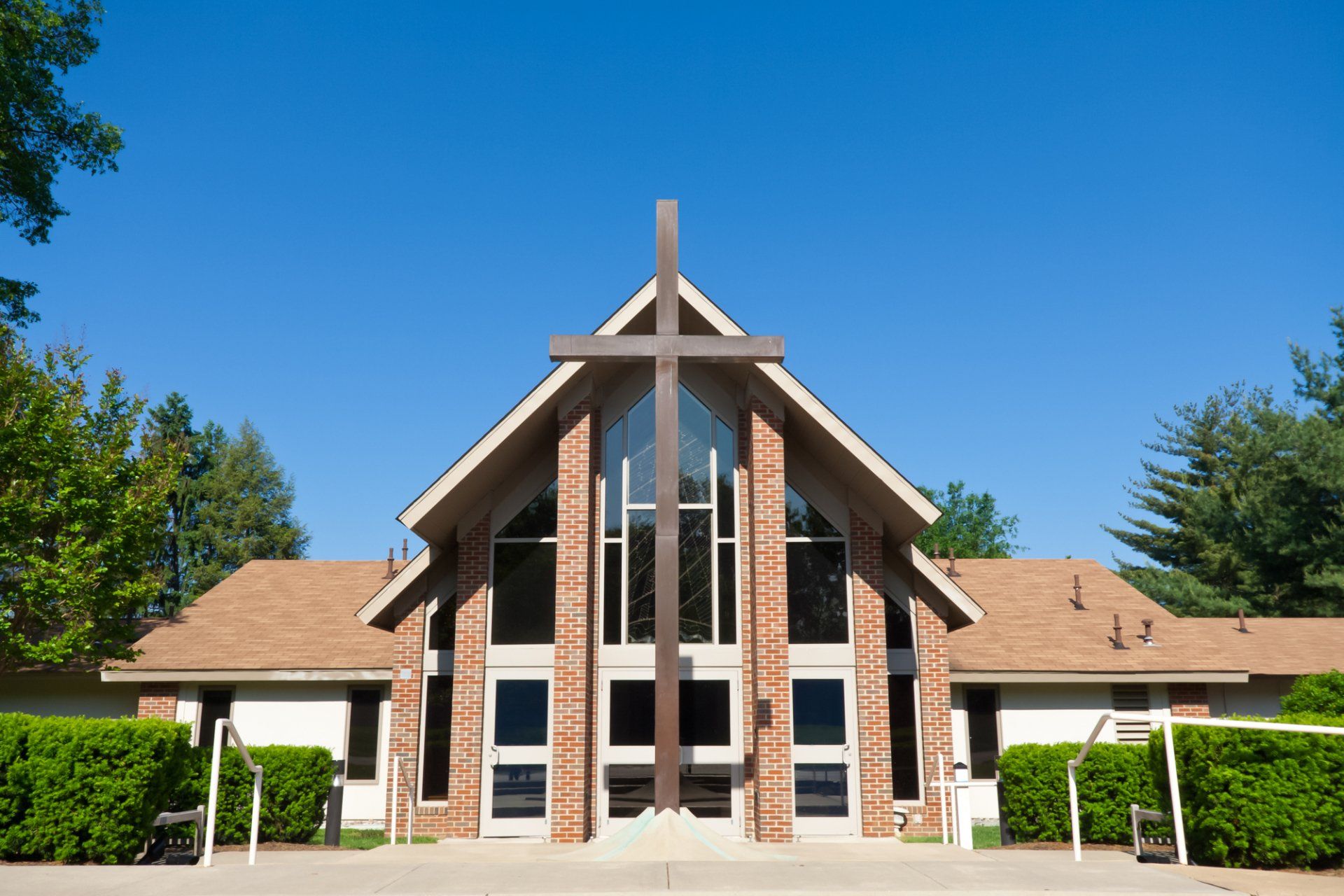 Church building with large wooden cross. Brown roof, brick and white siding, blue sky.
