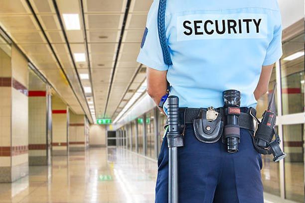 Security guard in uniform with equipment, standing in a brightly lit hallway.
