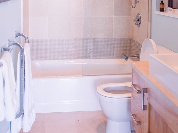 Bathroom with white tub, toilet, light wood vanity, and towels hanging.