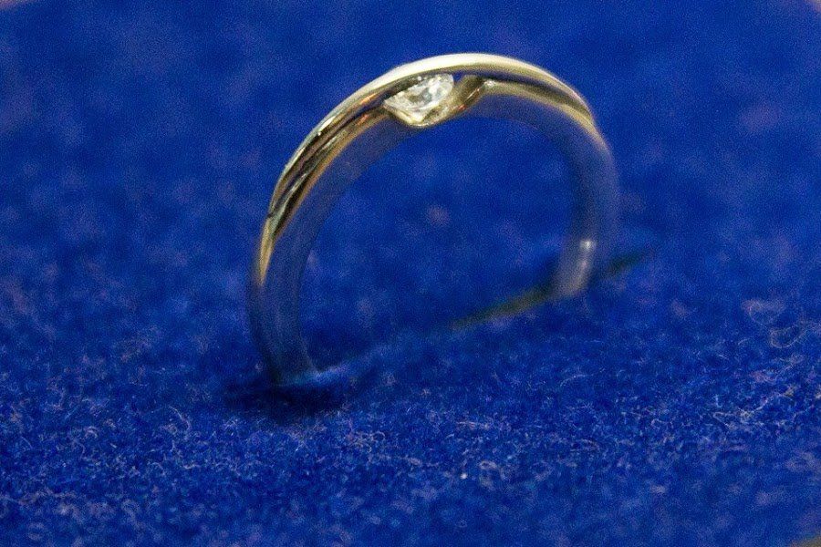 Um anel de ouro com um diamante no centro está sobre uma superfície azul