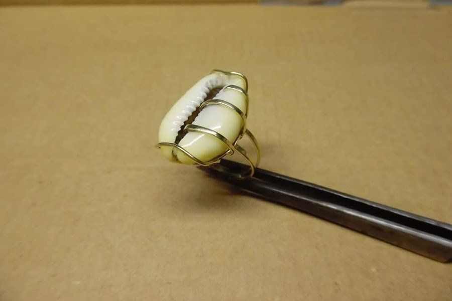 Um anel com uma concha está apoiado em uma pinça.