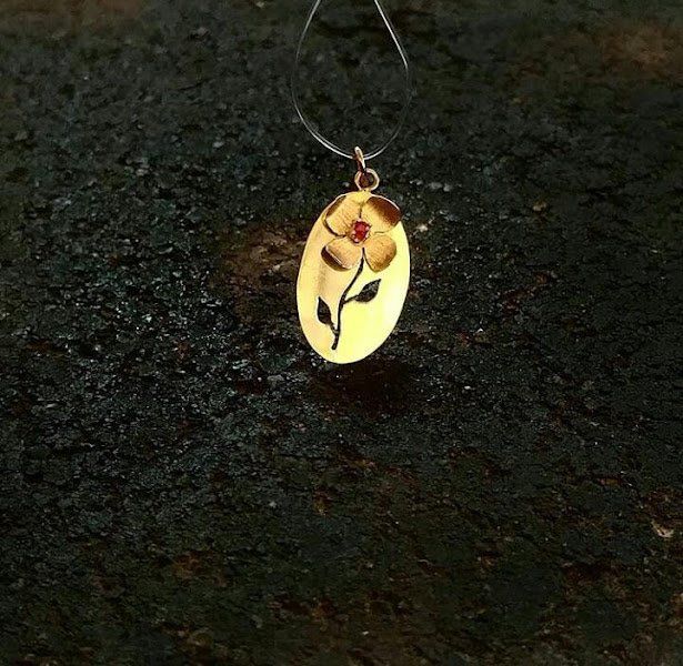 Um pingente de ouro com uma flor está sobre uma superfície preta.