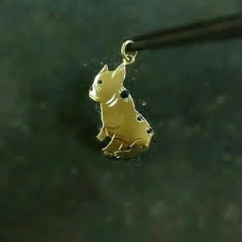 Um pingente dourado de buldogue francês está sendo segurado por uma pinça.