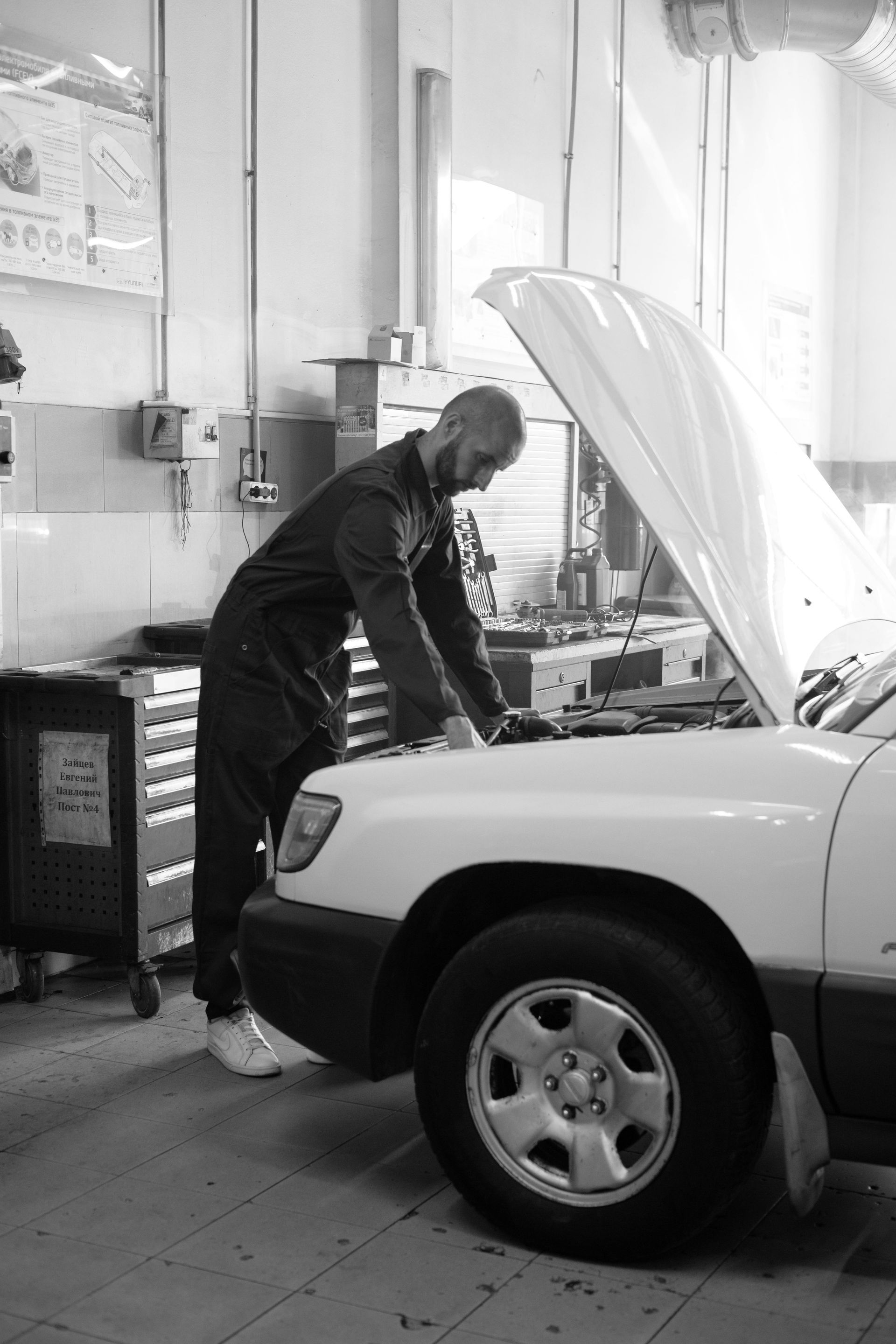 Mechanic working on a car engine, inspecting with a tool.