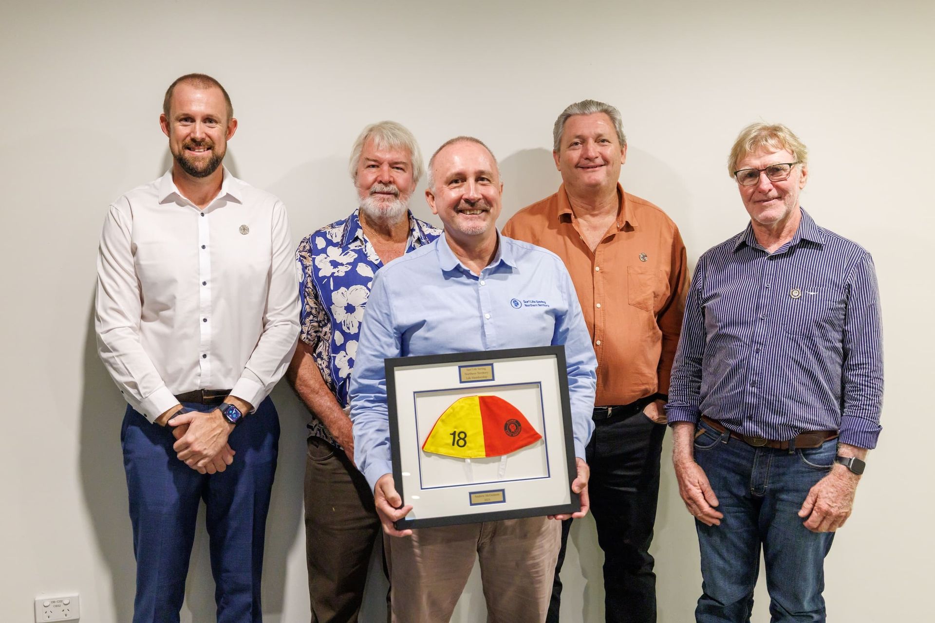 Five people stand indoors, with one holding a framed colorful artwork.