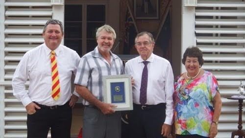 Four people posing outdoors, holding a framed award in front of a building.