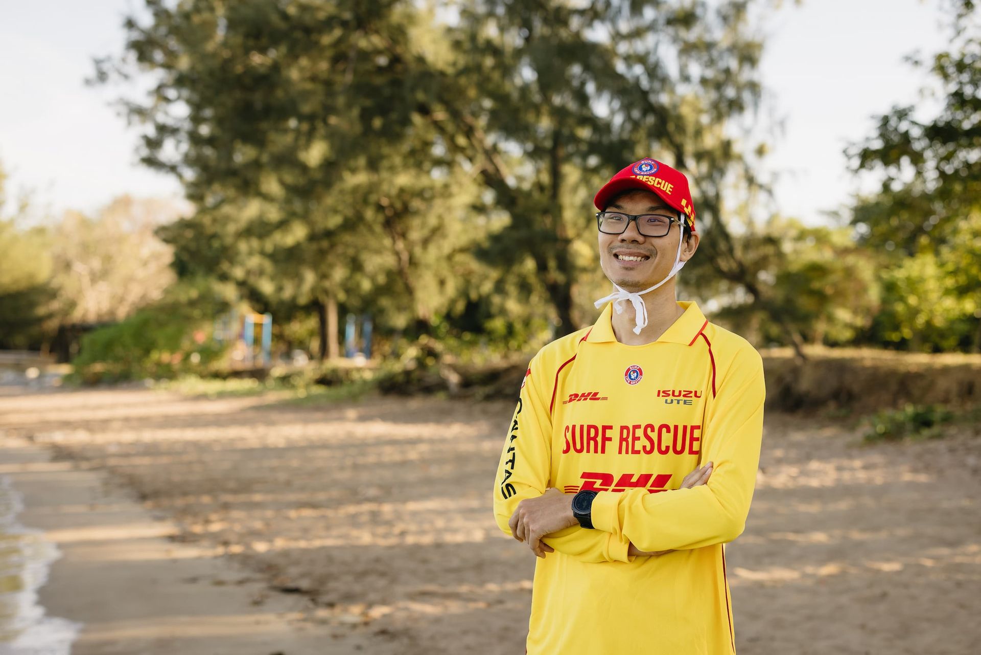 Life guard in yellow uniform and red cap standing outdoors with arms crossed