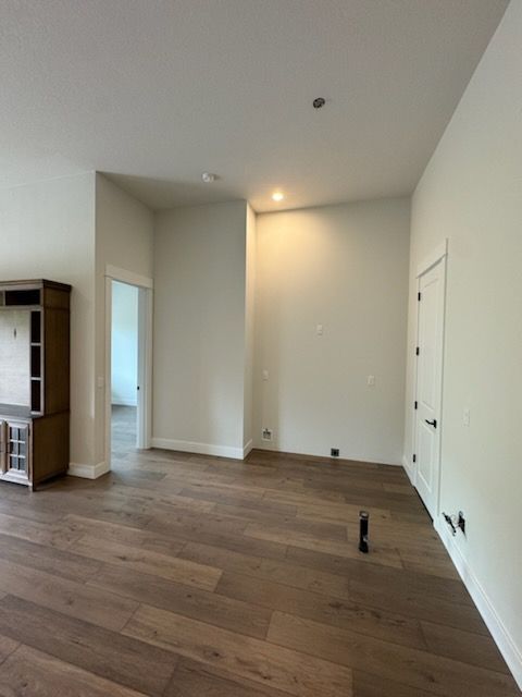 Empty room with hardwood floors, white walls, and a wooden cabinet. A door is visible.