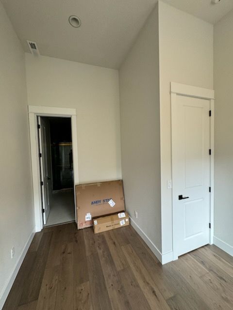 Empty room with wood floor, white walls and trim, door on the right and left. Cardboard boxes sit on floor.