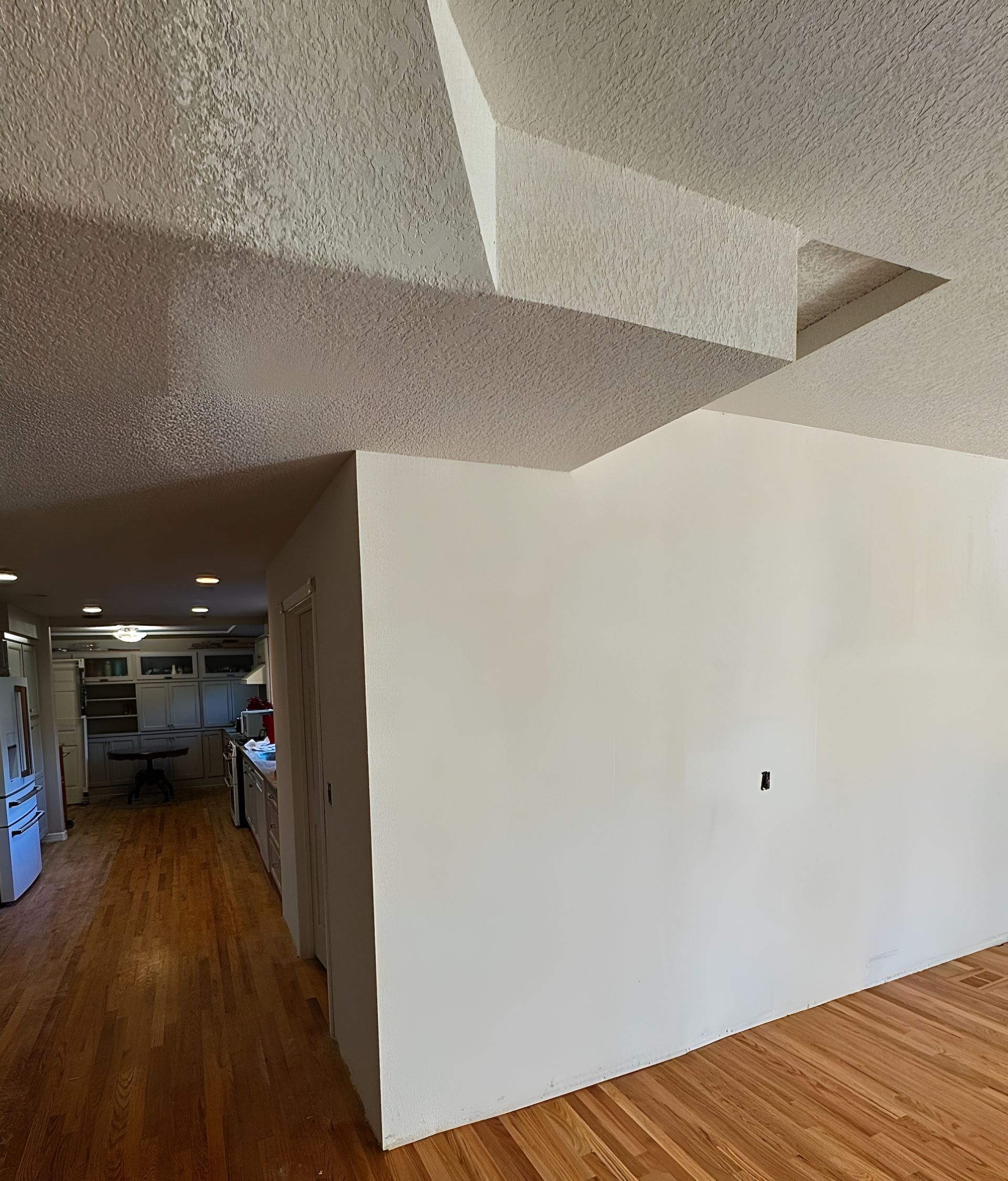 Room interior with white walls, textured ceiling, wooden floor, and hallway view.
