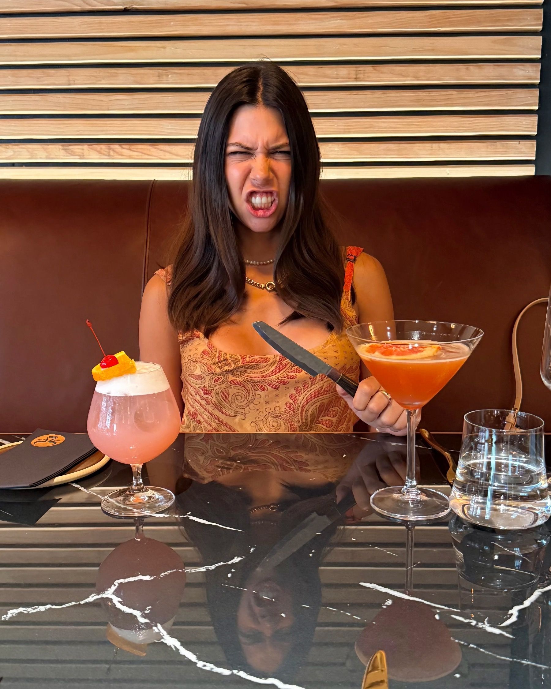 Paige Ellis Green holding a steak knife and two cocktails at East City Grill, playful reaction mid-lunch