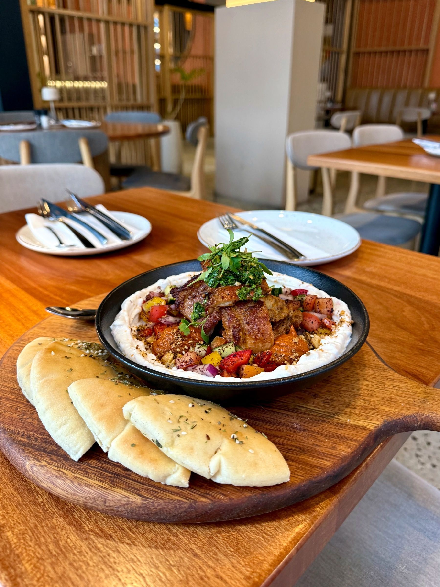 Hummus and meat dish with pita bread on a wooden board in a restaurant.