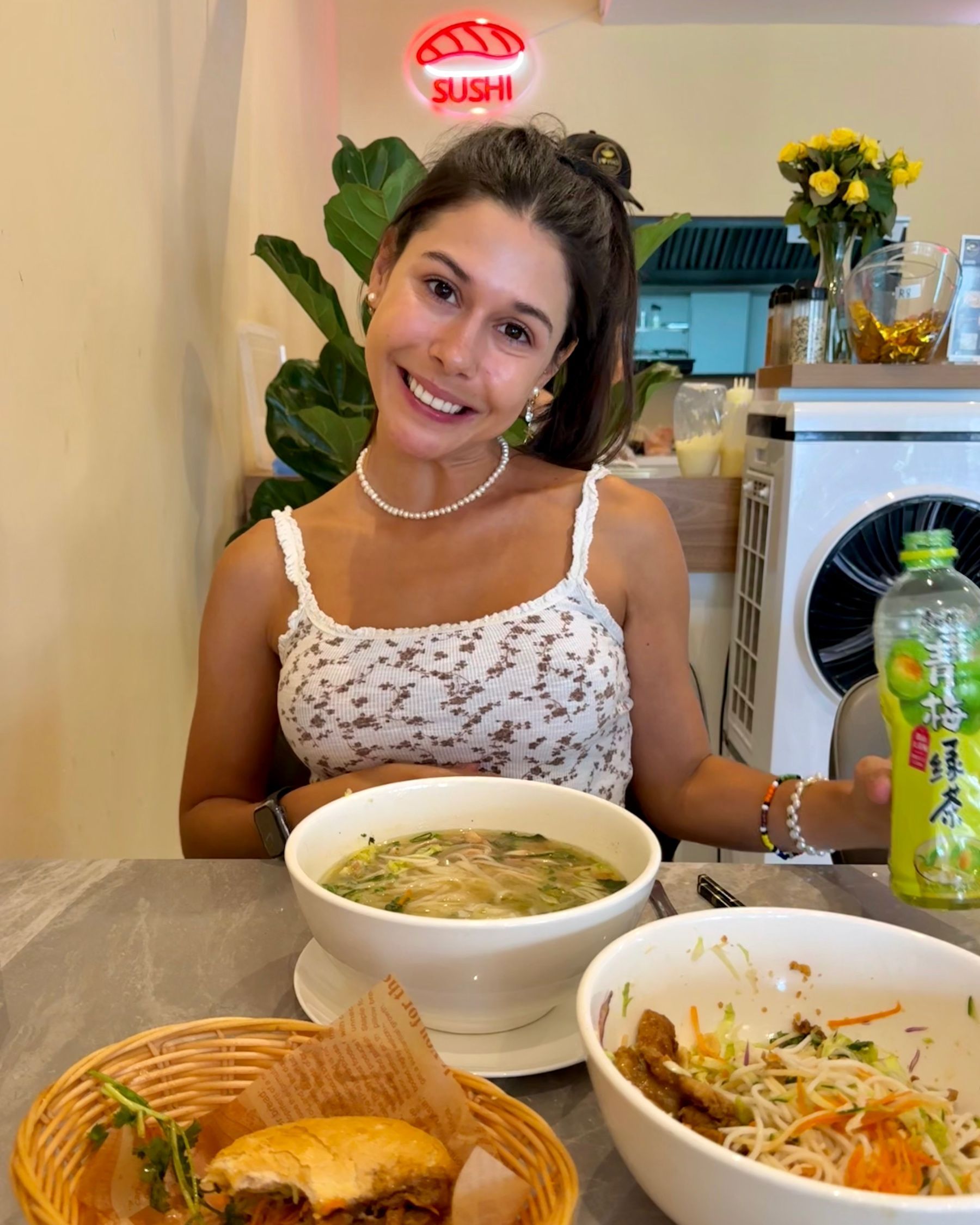Paige smiling with drink, pho and Vietnamese dishes