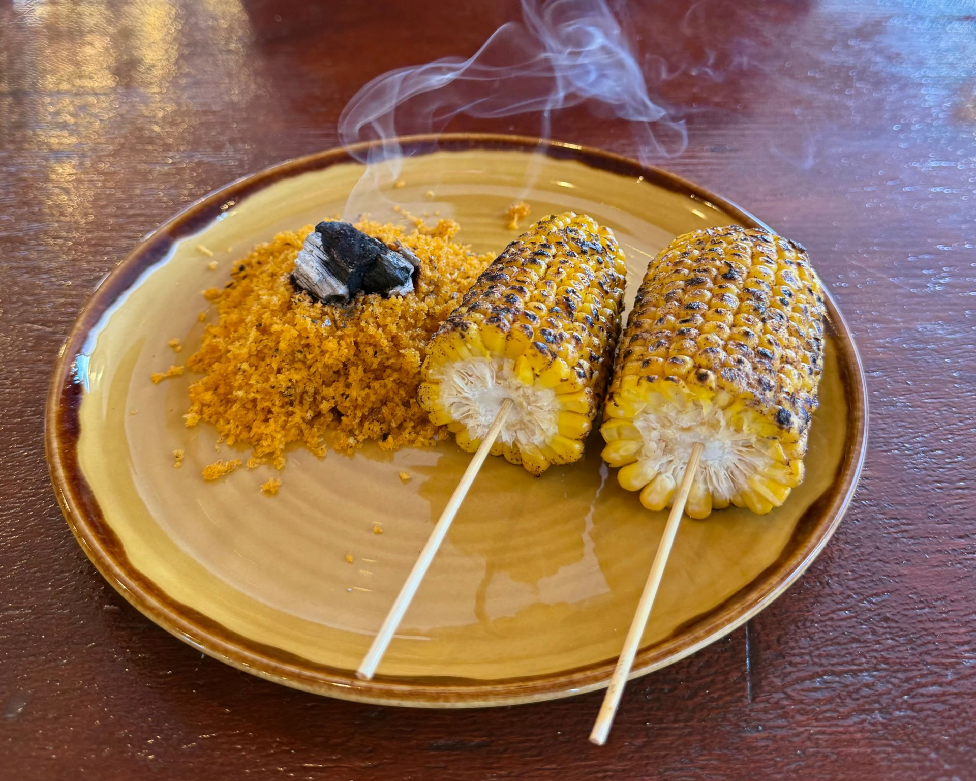 Grilled corn on the cob with spices, served on a plate, with smoke rising.