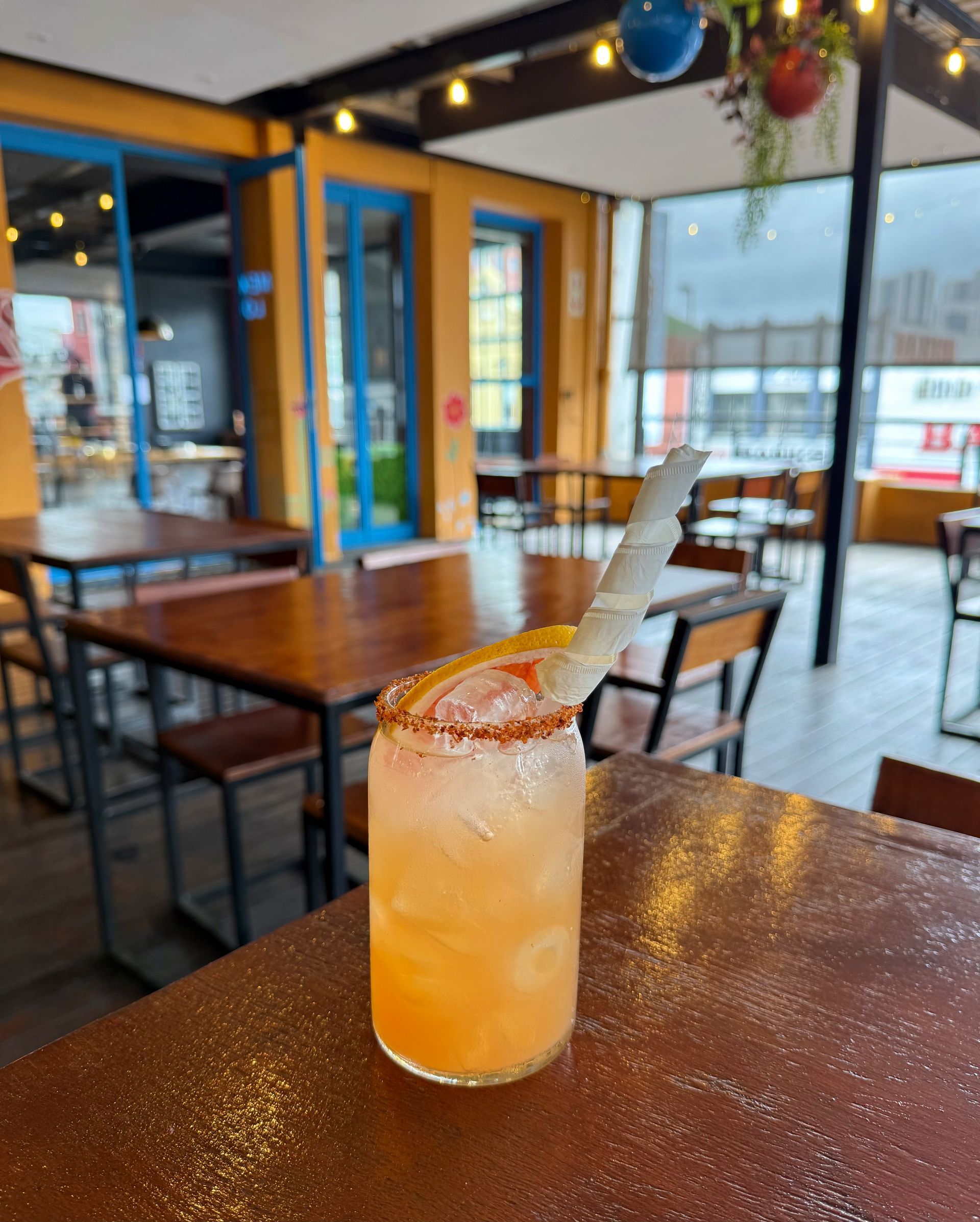Cocktail with orange slice garnish on a table at an outdoor restaurant with seating.