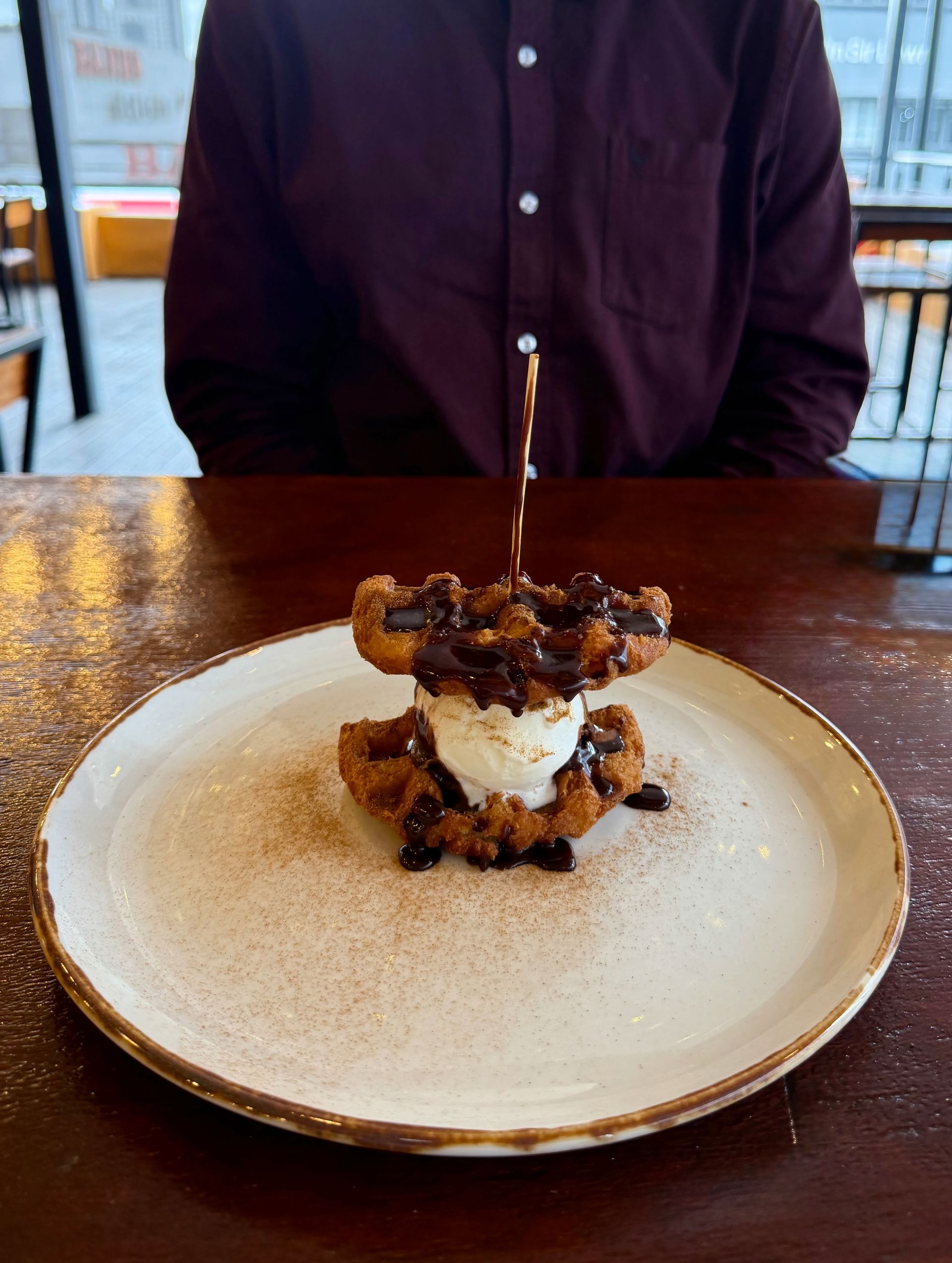 Waffles with ice cream and chocolate sauce on a plate, person in background.