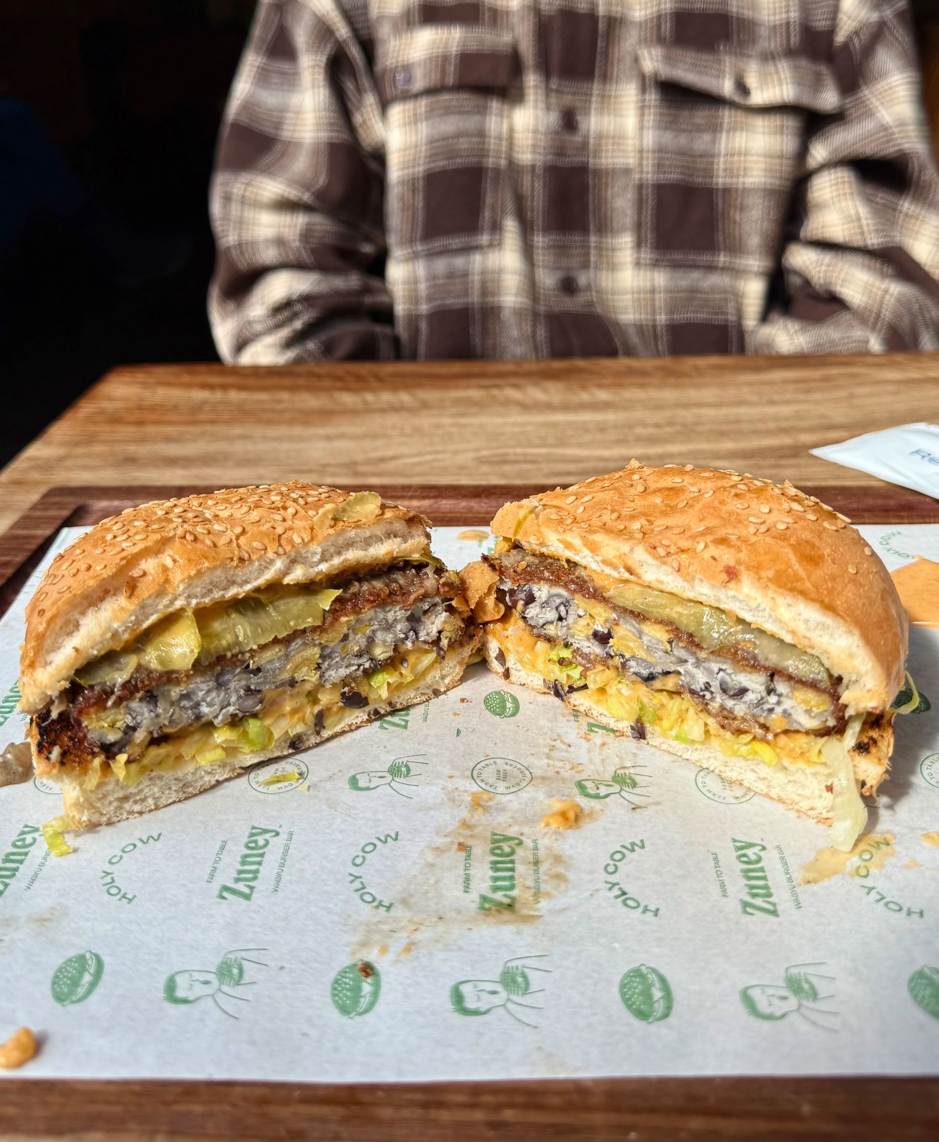 A burger cut in half, showing layers of patty, cheese, and toppings, on a sesame seed bun.
