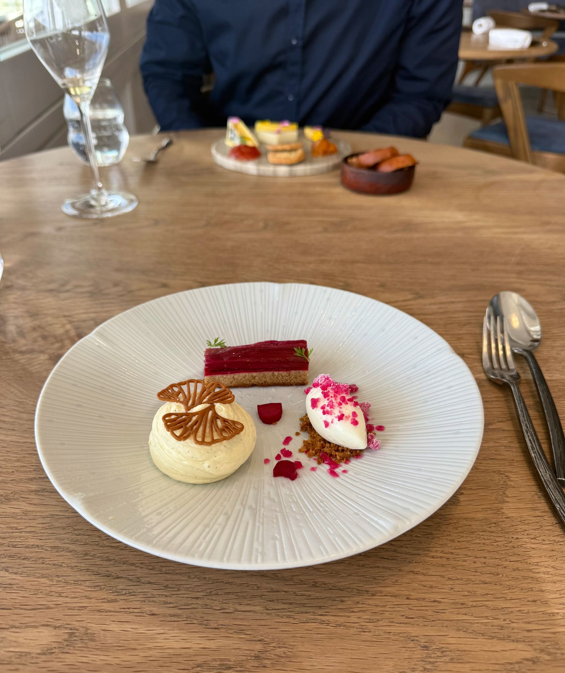 Dessert plate with cake, ice cream, and fruit on a wooden table, with a person in the background.