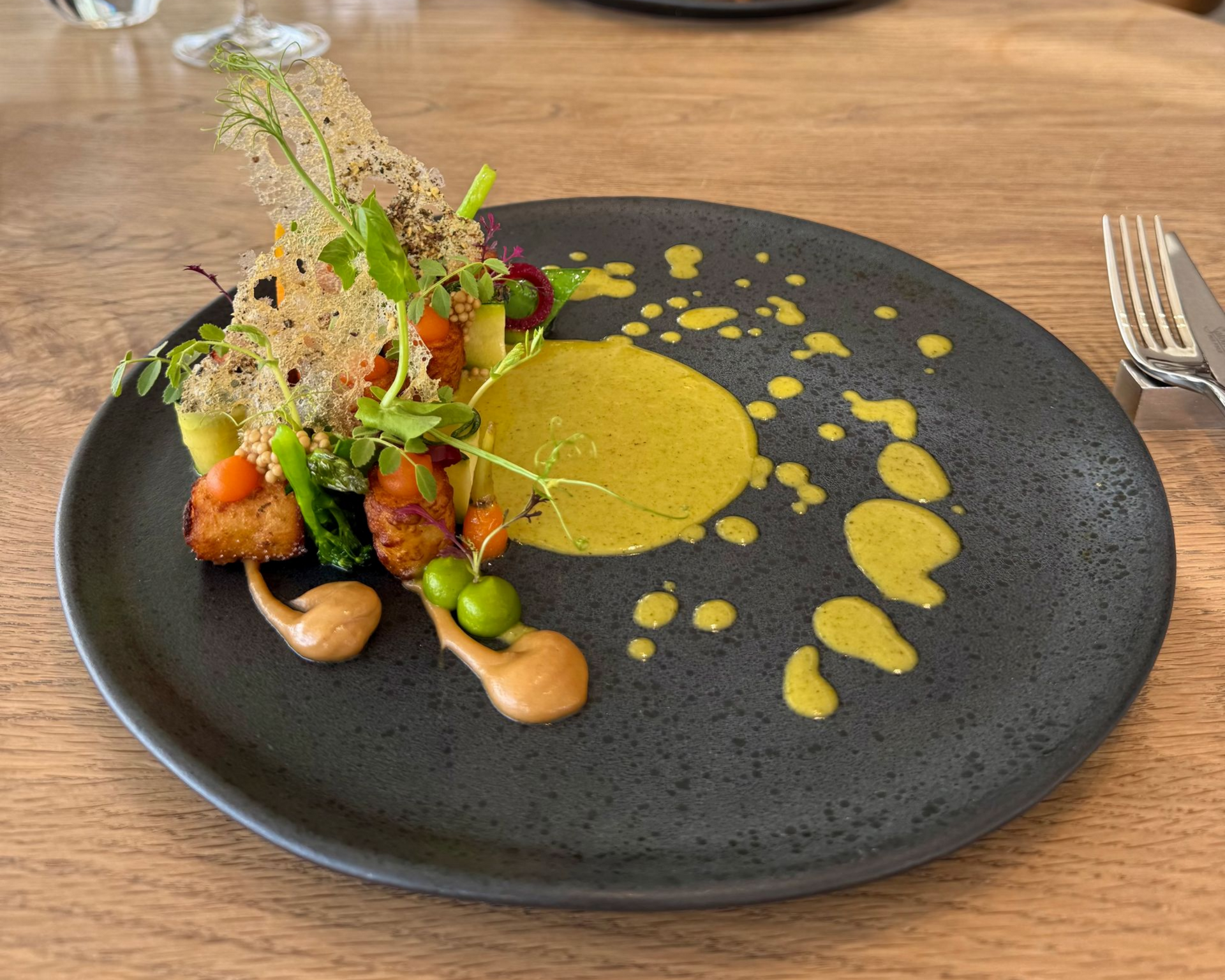 Gourmet plate with breaded food, yellow sauce, vegetables, and two brown dollops on a gray plate.