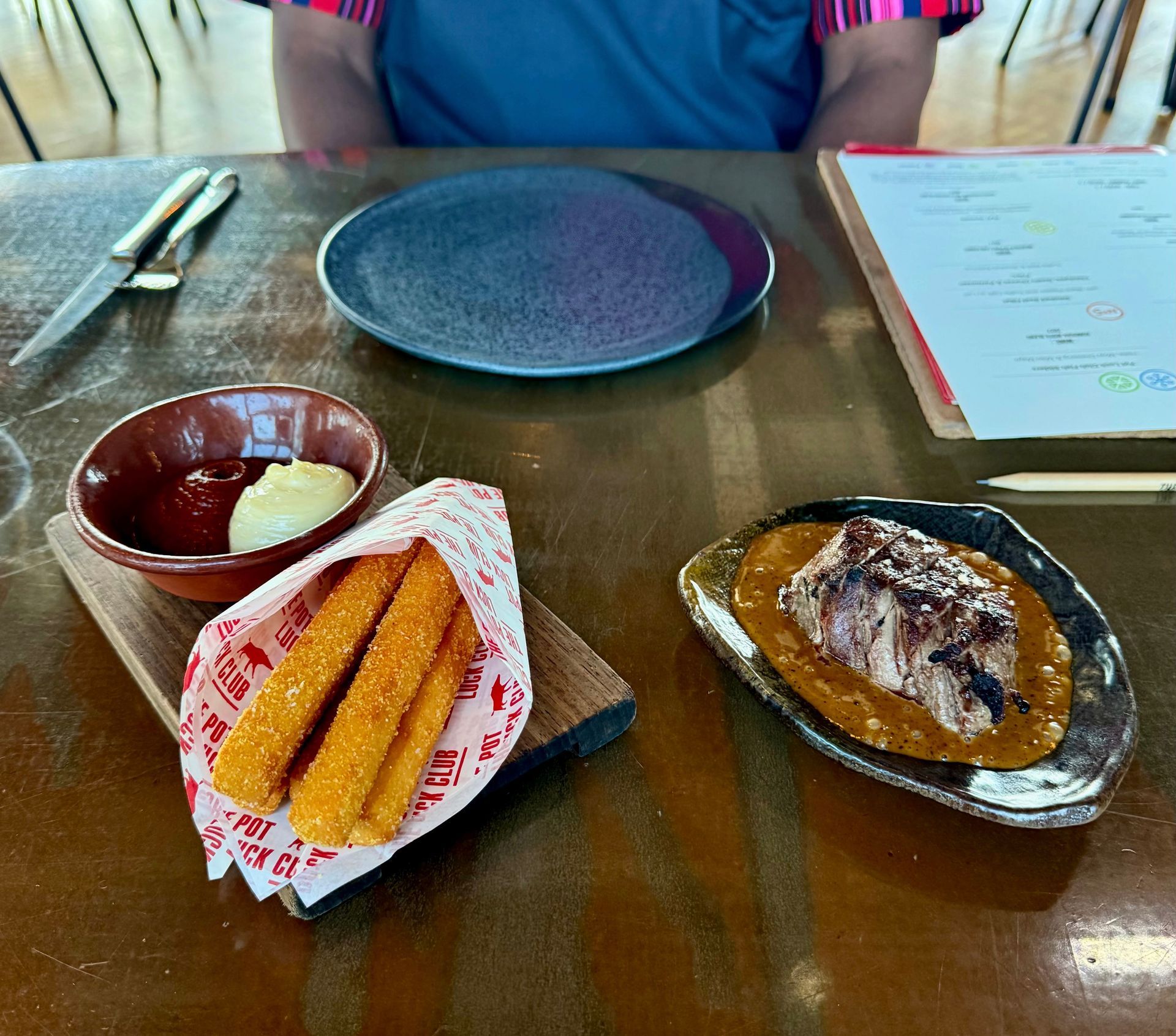 Table with appetizers: fries, dipping sauces, a small meat dish, and a menu.